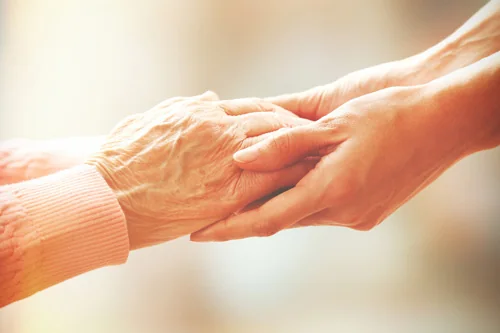 Betreuungskraft hält die Hand einer Seniorin zuhause – 24-Stunden-Betreuung der Märkischen Seniorenhilfe